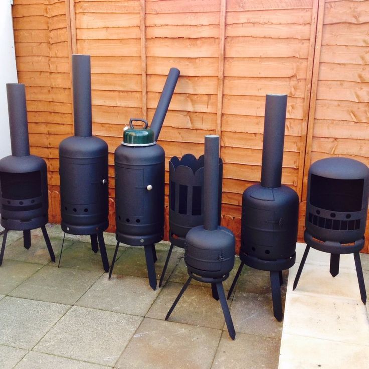 several black stoves sitting next to each other in front of a wooden wall and fence