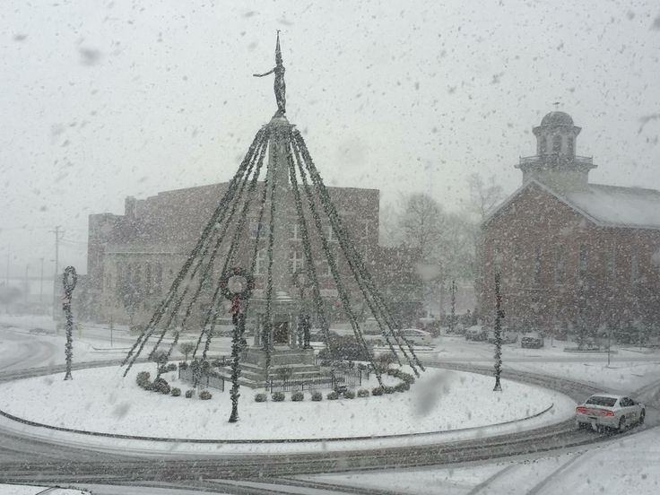 a very tall christmas tree sitting in the middle of a snow covered street