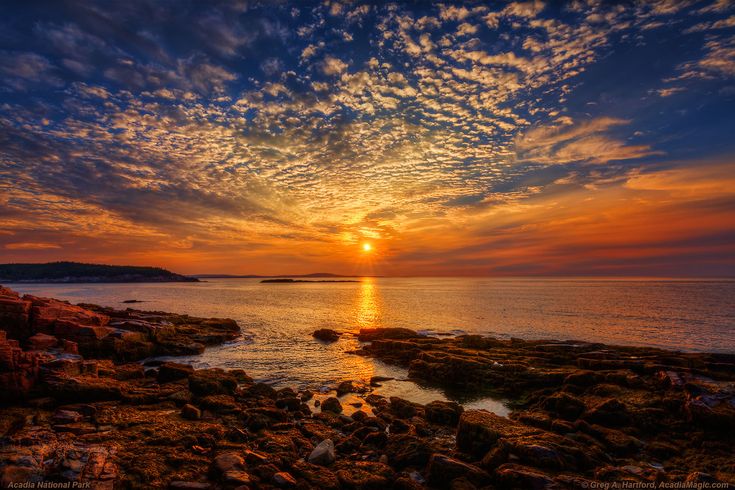 the sun is setting over the ocean with rocks in front of it and some water