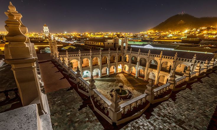 an old building is lit up at night with lights on the buildings and mountains in the background