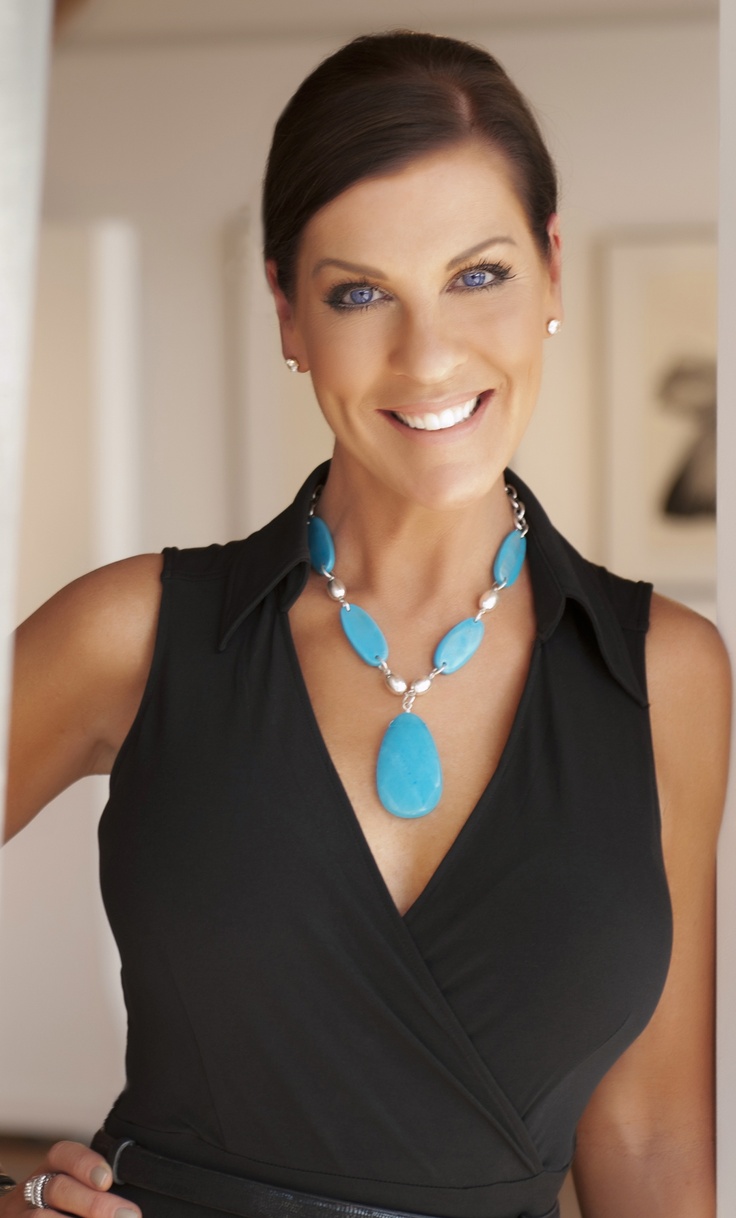 a woman wearing a blue necklace and black dress posing for the camera with her hands on her hips