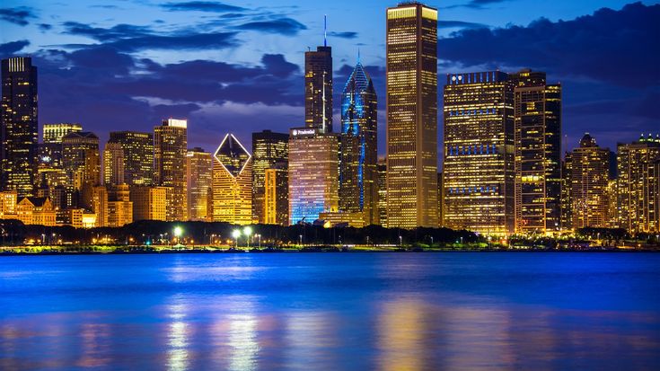 the city skyline is lit up at night, reflecting off the water and clouds in the sky