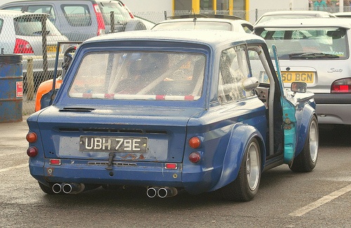 an old blue car is driving down the street with other cars behind it in traffic