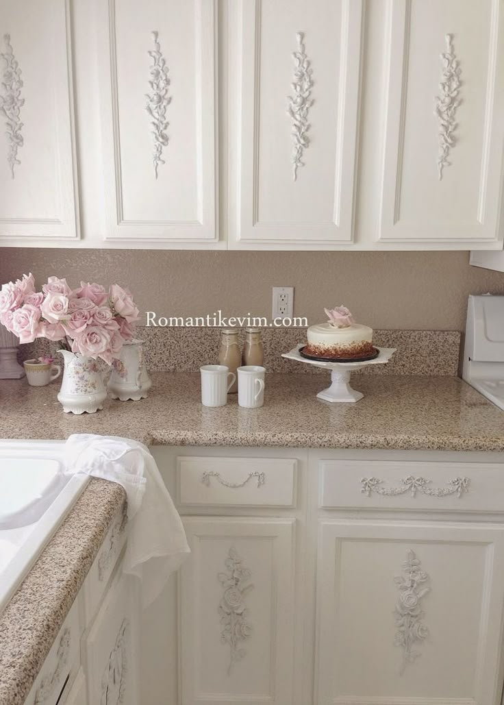 a kitchen with white cabinets and pink flowers on the counter