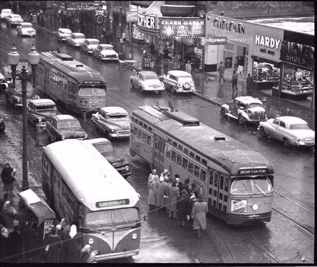 an old black and white photo of people standing on the sidewalk in front of buses