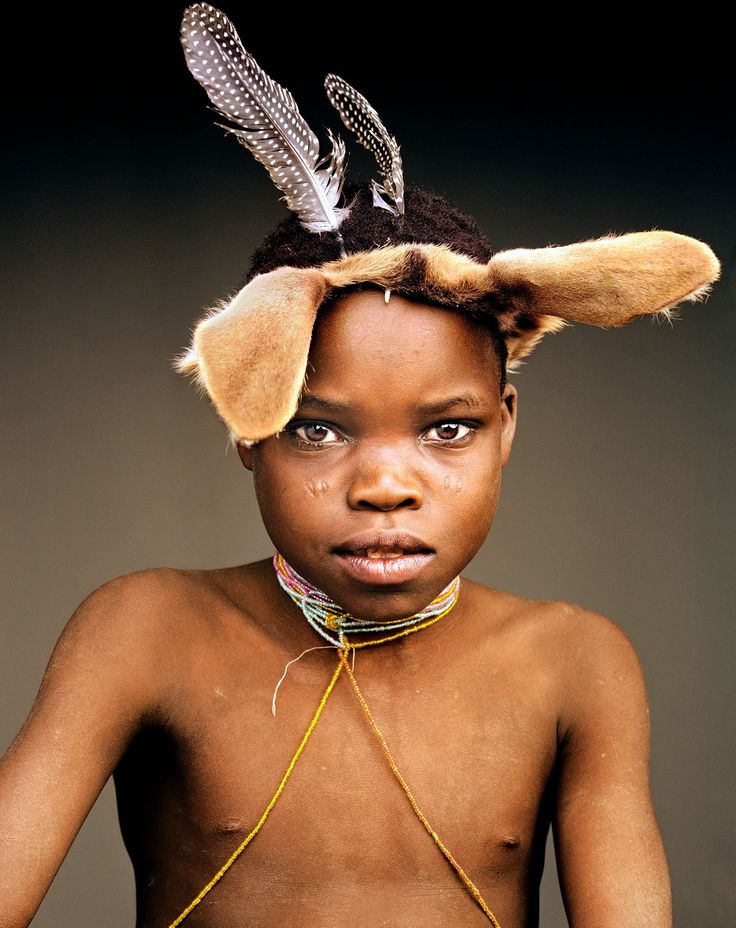 a young boy with feathers on his head is posing for the camera in front of a dark background