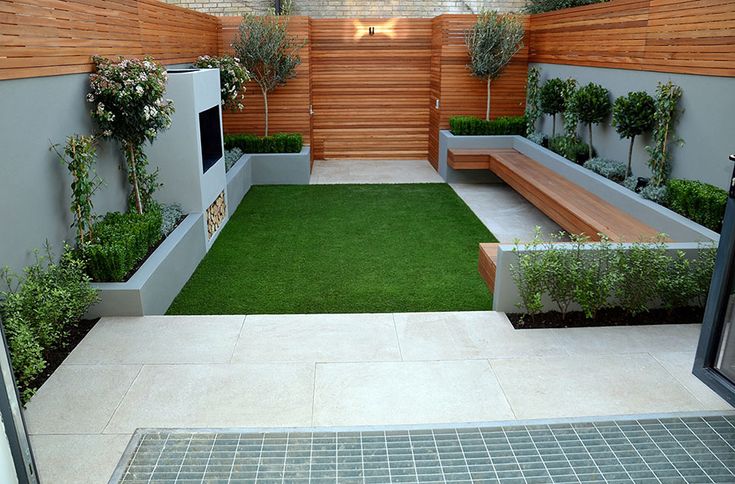 a small backyard with grass and wooden fenced in areas that include plants, benches and trees