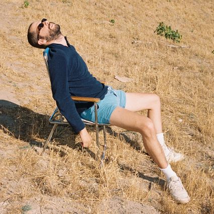 a man laying on top of a chair in the middle of a dry grass field