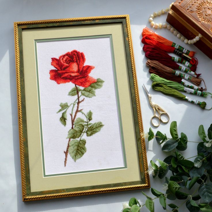 a red rose is in a frame next to some beads and other crafting supplies