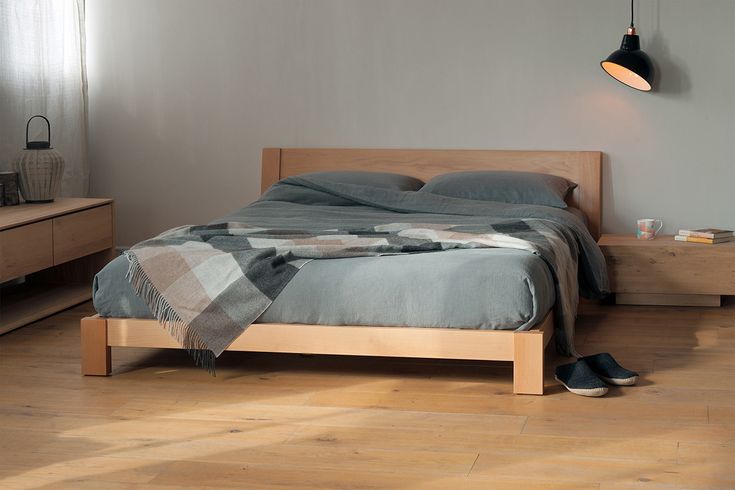 a bed sitting on top of a wooden floor next to a dresser and lamp above it