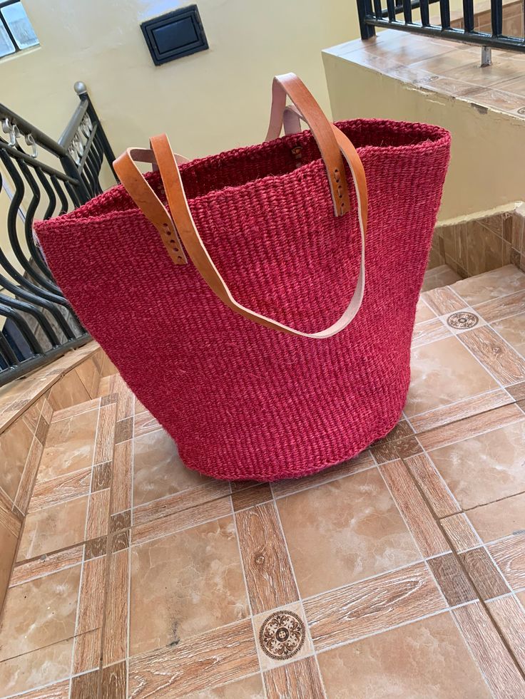 Kiondo overview A beautiful hand made kiondo bag in Cherry red color. A wonderful art piece for your everyday activities and a great gift for a loved one. The bag is made of sisal fiber that is hand picked hand prepared into yearn then twisted and weaved. It is finished with natural leather mainly from cow hide. Uses Day out: Its a great bag for use in carrying personal effects such as outdoor mats,sandals and other picnic items Shopping: The bag has large space that can adequately accommodate y Shopping Bucket Beach Bag With Handles, Red Beach Bag With Double Handle, Red Bucket Bag For Everyday Use, Handmade Red Bucket Crochet Bag, Red Leather-handled Bucket Bag, Red Handwoven Rectangular Straw Bag, Handmade Red Crochet Bucket Bag, Red Leather Handle Bucket Bag, Red Handmade Crochet Bucket Bag