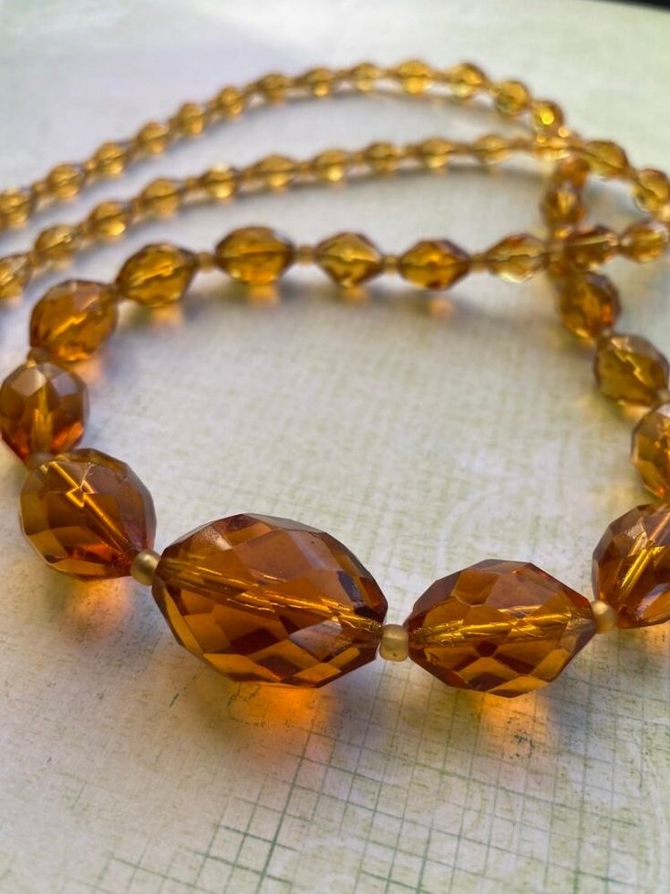 an orange necklace is sitting on a white tablecloth and it has yellow glass beads hanging from the bead