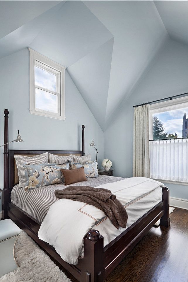 a bedroom with blue walls and wooden floors has a large bed in the corner, along with two windows