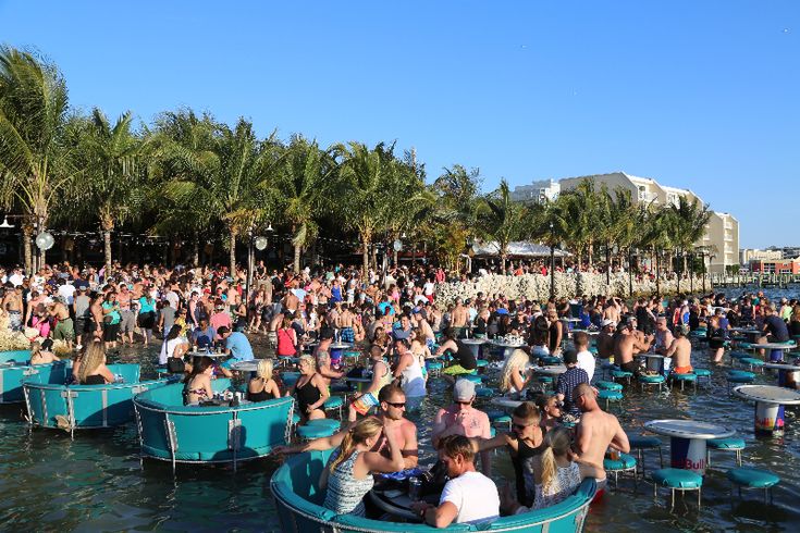 a large group of people are sitting in small boats on the water, with palm trees behind them