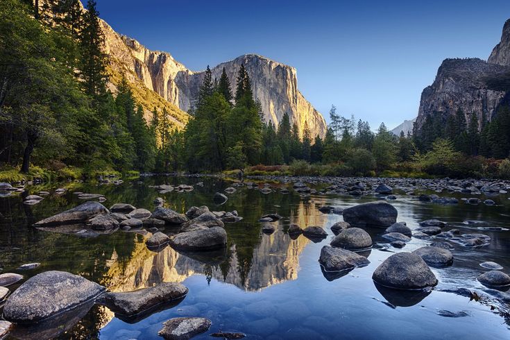 a river surrounded by mountains and trees with rocks in the water