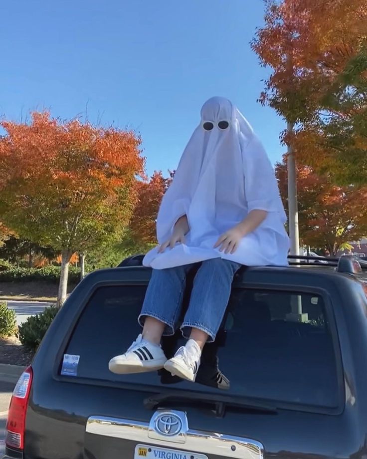 a person sitting on the back of a car wearing a white sheet over their head