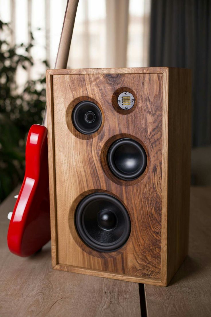 a wooden speaker sitting on top of a table next to a red phone and plant