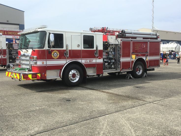 a red fire truck parked on top of a parking lot next to other trucks and people