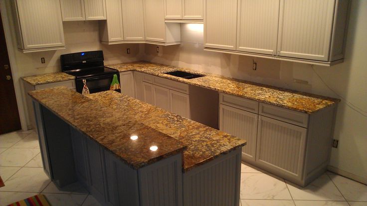 an empty kitchen with granite counter tops and white cupboards on either side of the island