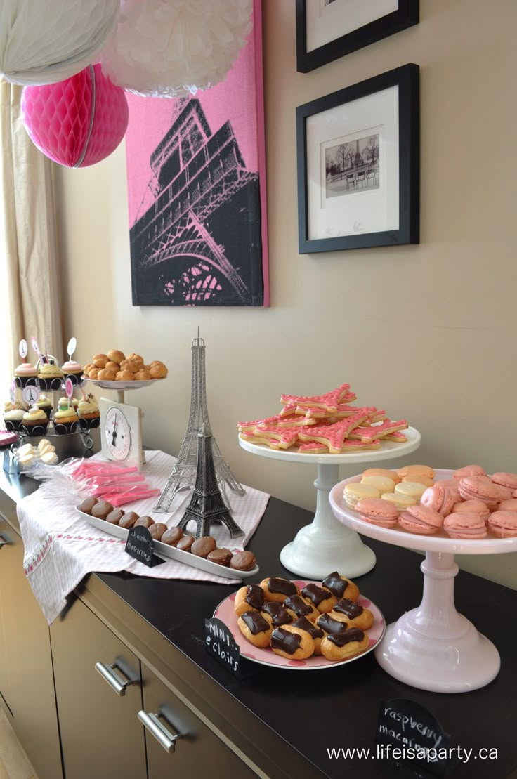 a table topped with lots of pastries next to a wall mounted eiffel tower