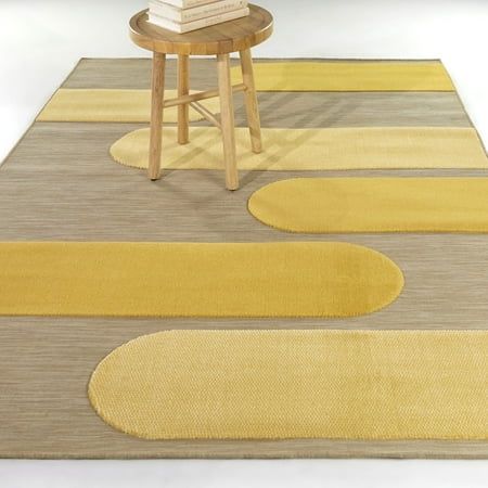 a yellow and gray area rug with circles on the floor next to a small stool