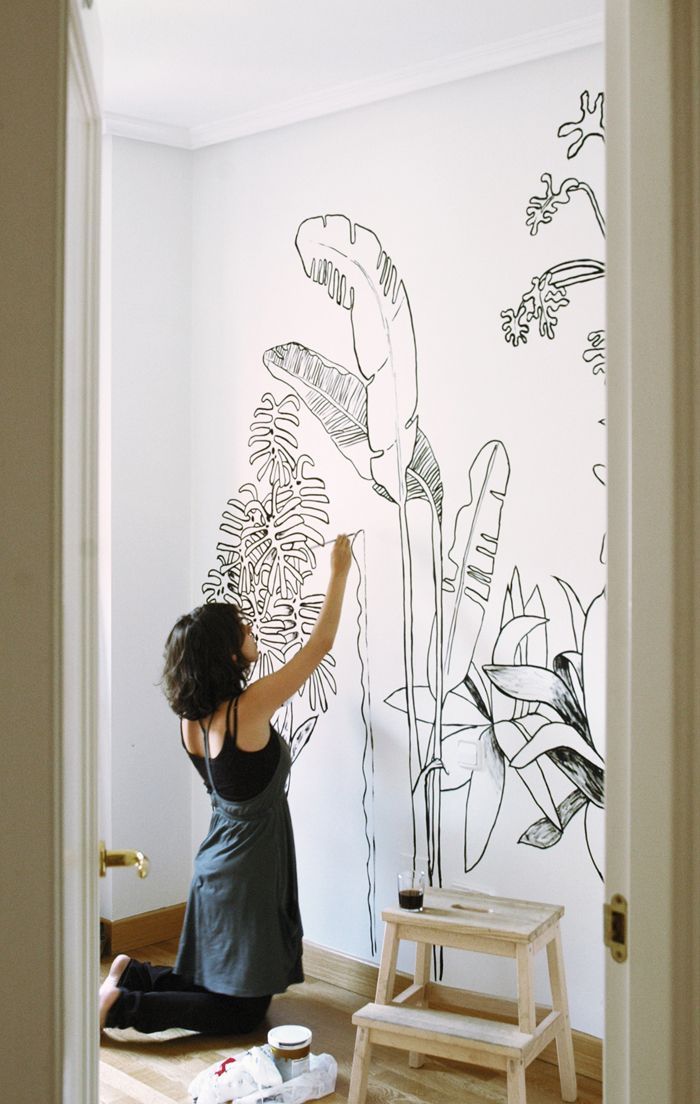 a woman sitting on the floor in front of a wall with plants drawn on it