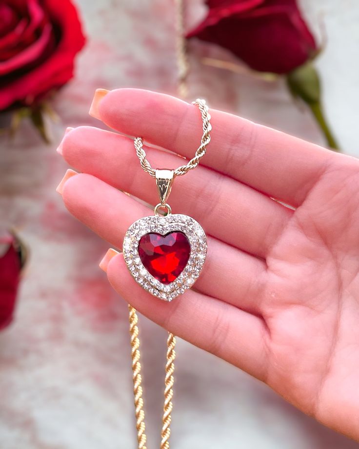 a person holding a red heart shaped necklace in their hand with roses behind it and the words, i love you