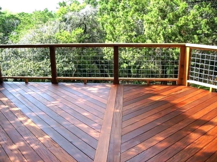 a wooden deck with metal railing and trees in the background