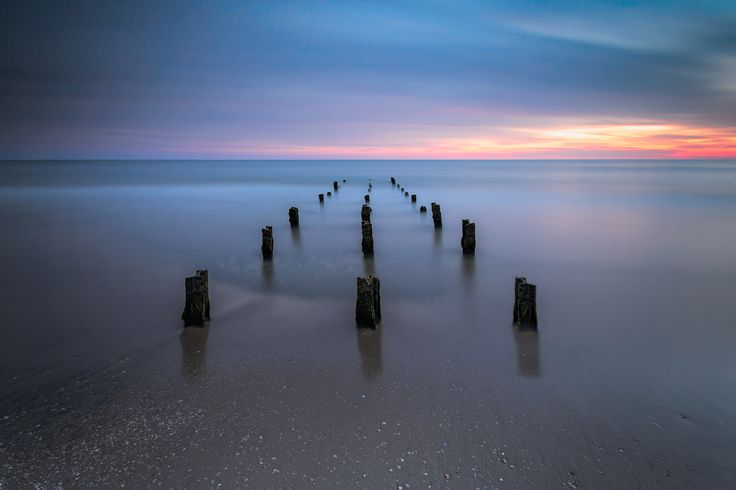 a long exposure photo of the ocean with old wooden posts sticking out of the water