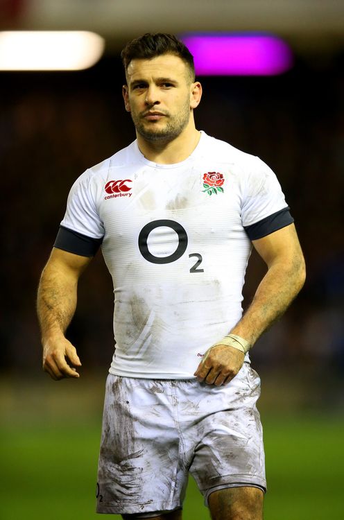 a rugby player standing on the field with his hands in his pockets and looking at the camera