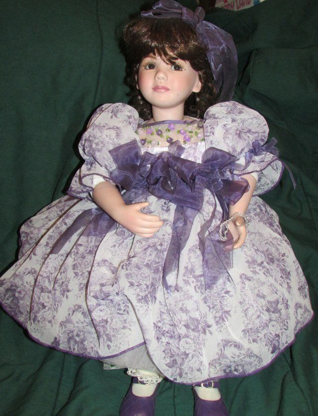 the doll is wearing a purple dress and hat