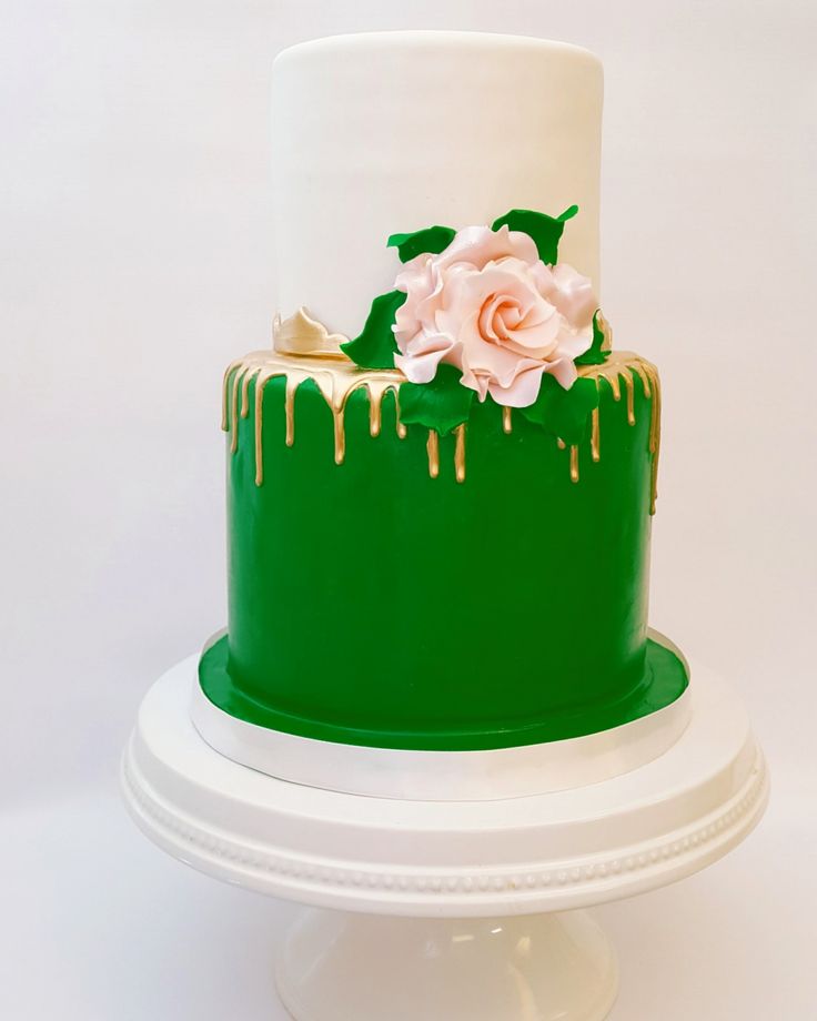 a green and white cake with flowers on top is sitting on a pedestal in front of a white background