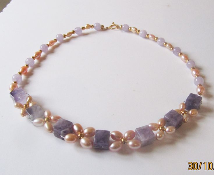 Pearl and Amethyst necklace woven into a floral pattern. Large cube of Amethyst has been woven with graduated sized rice Cultured Freshwater pearls in a lovely Apricot/Peach colour. The largest ones are at the front and measure 6x9mm to 7/8x5mm. The overall effect is a vintage style necklace with high visual impact.The cubes of Amethyst are substantial and measure 10mm. The other Amethyst are rounds and measure 8mm. They are matched with rice pearls measuring graduated from 9x6mm to 8x5mm. All t Elegant Lavender Beaded Necklace With Natural Stones, Purple Pearl Jewelry With Natural Stones, Elegant Lavender Necklaces With Gemstone Beads, Handmade Elegant Amethyst Beaded Necklaces, Purple Pearl Jewelry With Gemstone Beads, Handmade Purple Pearl Necklace For Gift, Elegant Handmade Lavender Necklaces, Handmade Delicate Purple Necklace, Purple Pearl Single Strand Necklace