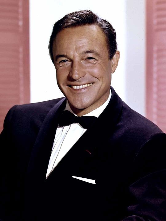 a smiling man in a tuxedo and bow tie posing for a photo with pink curtains behind him