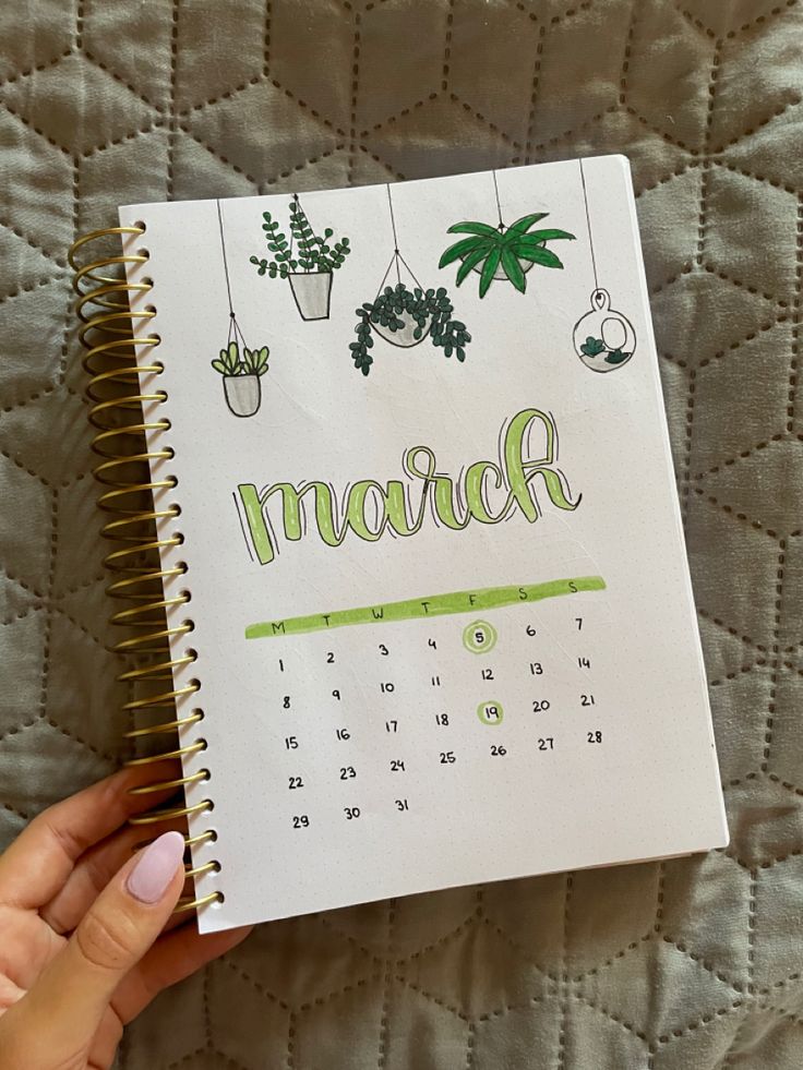 a hand holding a notebook with the word march written in green ink on it and hanging potted plants