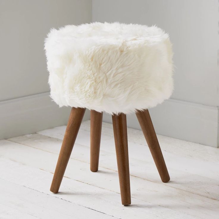 a white stool with wooden legs and a sheepskin seat cover on top of it