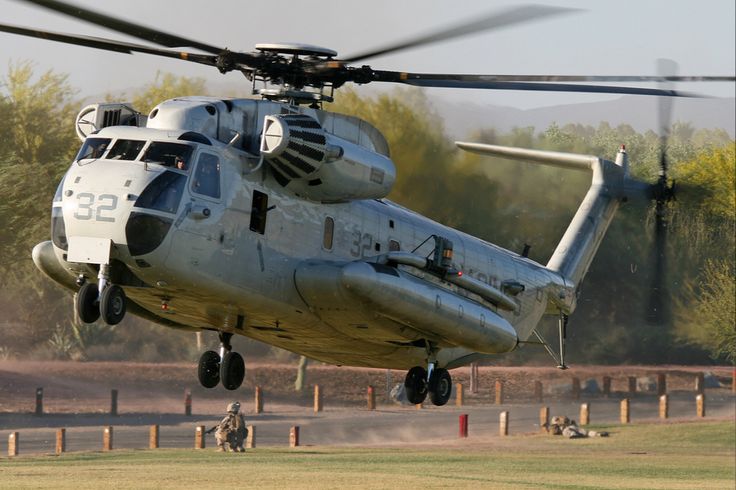 a helicopter that is flying in the air with people standing around it and trees behind it