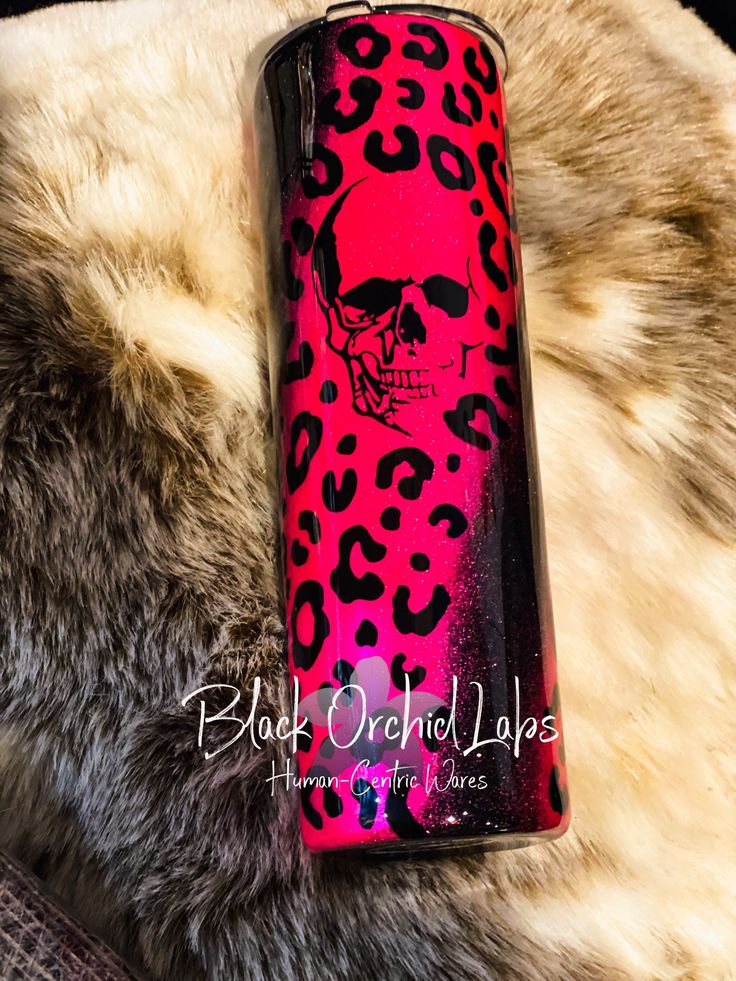 a pink and black leopard print lighter with a skull on the side, sitting on a fur covered surface