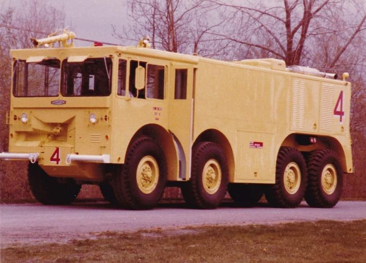 an old yellow fire truck is parked on the side of the road in front of some trees