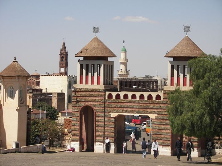 several people are walking around in front of an old brick building with two towers on top