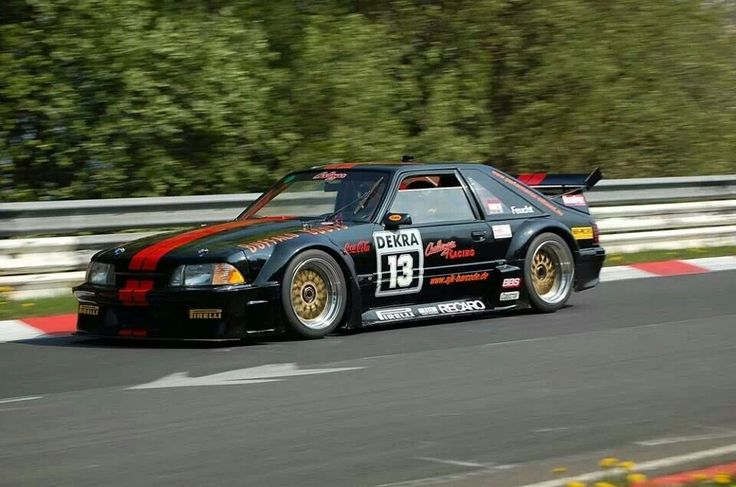 a black car driving on a race track with trees in the backgrouund