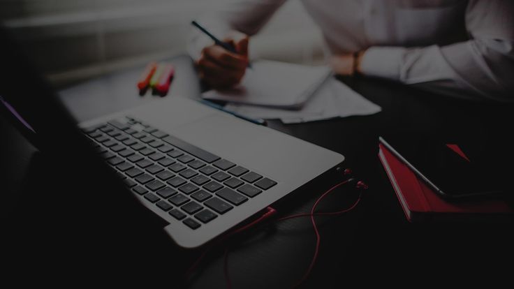 a person sitting at a desk writing on a notepad with a laptop in front of them