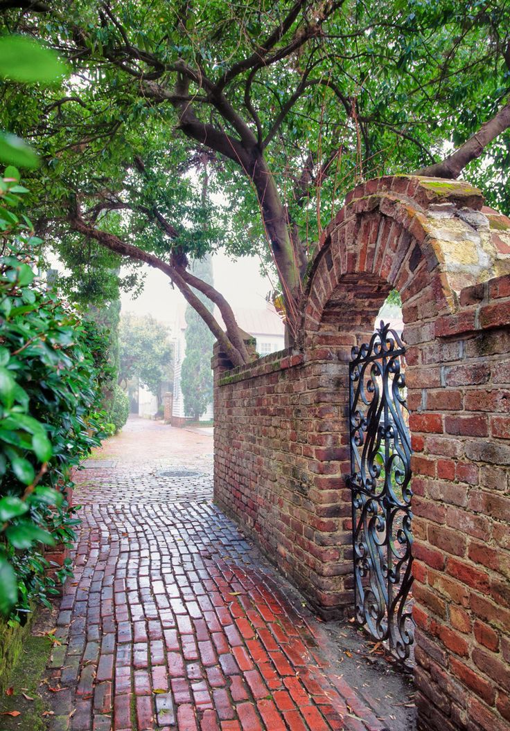 an iron gate on the side of a brick wall next to a tree and walkway