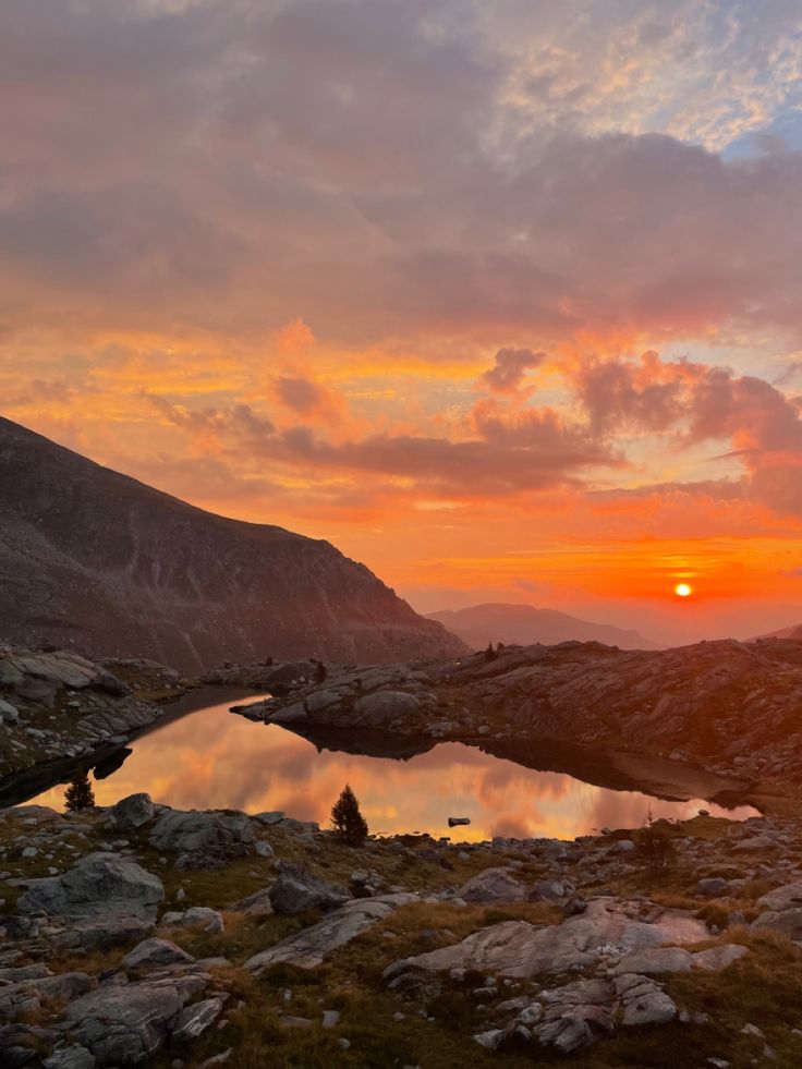 the sun is setting over a mountain lake