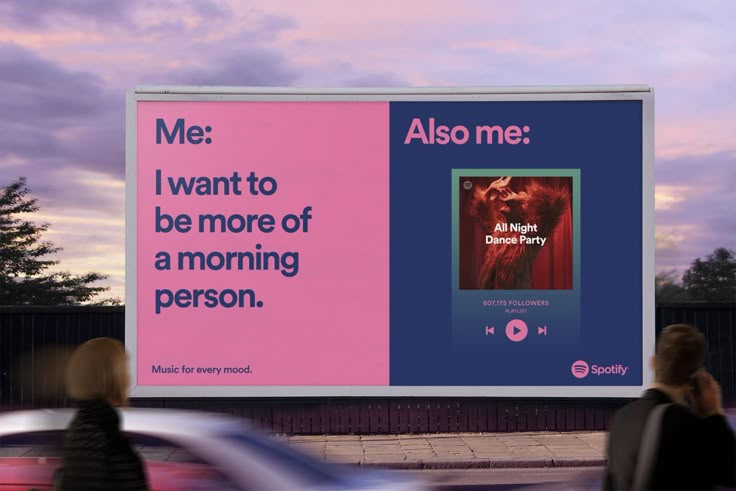 two people walking past a large billboard on the side of a road that reads, me i want to be more of a morning person