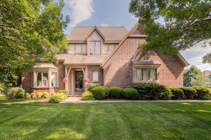 a large brick house in the middle of a green yard with trees and bushes around it