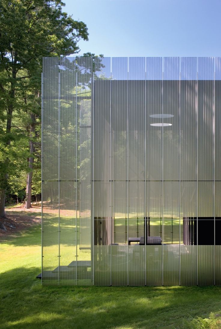 a glass structure in the middle of a grassy area with trees and grass behind it