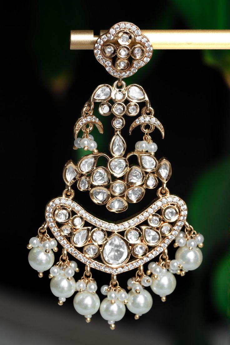 Embrace timeless elegance with our Chashni Chandbali kundan earrings: a masterpiece of traditional craftsmanship and contemporary allure. A stunning piece of unique South Asian jewelry, Chashni is an elegant 21K gold plated chandelier earring adorned with a shimmering Alhambra motif, dangling mini crescents, and lustrous pearls. Chashni's kundan stones are meticulously hand-set by master artisans to create an ethereal array of light that dazzles in every environment. Enhance even your most elega Luxury Chandbalis With Intricate Design For Diwali, Luxury Fusion Style Chandbalis For Wedding, Luxury Chandbalis With Intricate Design For Reception, Luxury Temple Jewelry Chandbali Bridal Sets, Luxury White Chandbali Pearl Necklace, Luxury Traditional Chandbali Pearl Earrings, Luxury Hand Set Chandbali Chandelier Earrings, Luxury Chandbali Pearl Earrings With Intricate Design, Cheap Traditional Chandbali Jewelry