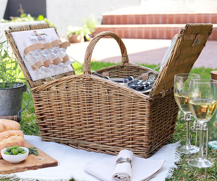 two wicker picnic baskets sitting on top of a grass covered field next to wine glasses