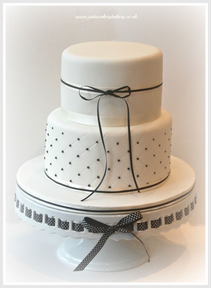 a three tiered white cake with black dots and ribbons on it's sides